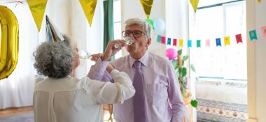 Senior couple links arms to drink champagne at a party